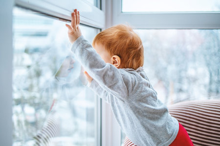 the kid carefully looks out the window at the snow and what is happening around, side view, close-up with space for text.の写真素材