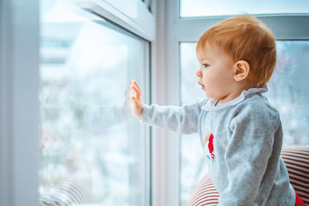 the kid carefully looks out the window at the snow and what is happening around, side view, close-up with space for text.の写真素材