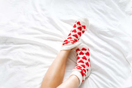 womens feet in warm socks with red hearts on a white bed.の写真素材