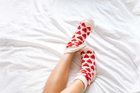 womens feet in warm socks with red hearts on a white bed.の写真素材