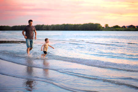 dad runs after his son along the riverbank at sunset.