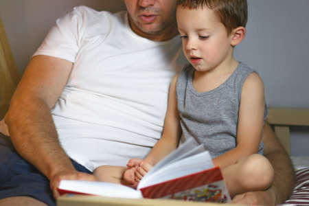evening family reading. a father reads a book to his son before going to bedの写真素材