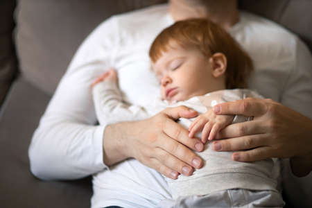 Toddler and dad sleeping on the couch during the day, concept childrens day and Parental care. Focus on the hands.の写真素材