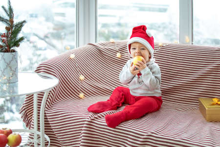 Toddler bites apple sitting on sofa indoors.の写真素材