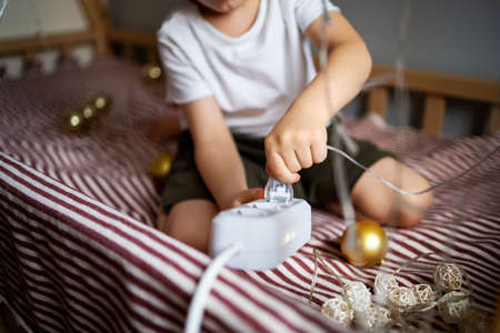 Child safety at home concept. The child inserts a plug into the socket to turn on the New Years garland.の写真素材