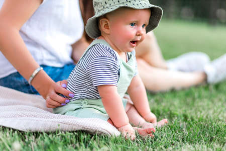 Cute fun baby in casual style sits on green grass with his mom, concept childhood.の写真素材