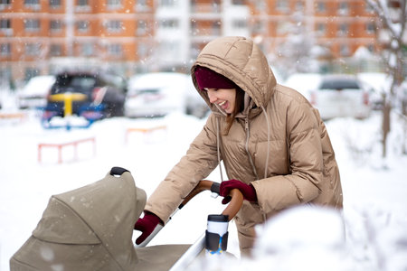 A young mother smiles at her child in a baby stroller on a walk on a winter day. concept motherhoodの写真素材