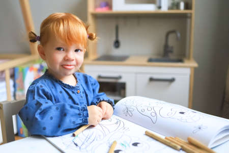 A little girl of a year and a half at home sits at a table and draws, admires.の写真素材