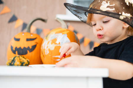 a little girl in a witch costume paints pumpkins for Halloween at home, the concept of childrens creativity.の写真素材