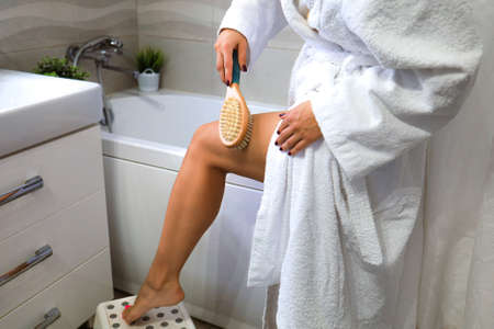 A young woman performs a massage with a wooden brush with natural bristles at home in the bathroom, the concept of body care.の写真素材
