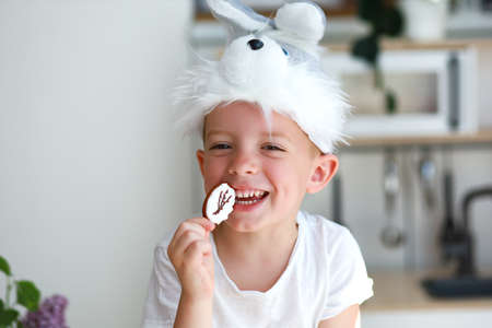 a boy in a rabbit costume eats Easter cookies in the form of an egg and laughs happily.
