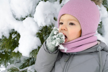 portrait close up cute toddler girl licking snowflakes outdoors in winter.