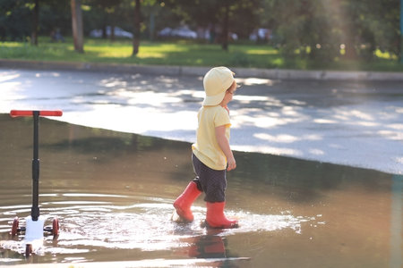 toddler 2 years enjoys a summer day, rides a scooter and walks through puddles in rubber boots.の写真素材