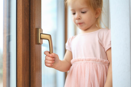 close-up portrait of a cute girl of 2-3 years old holding her hand by the handle of the window inside the room.の写真素材