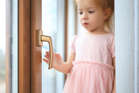 close-up portrait of a cute girl of 2-3 years old touch by the handle of the window inside the room.の写真素材
