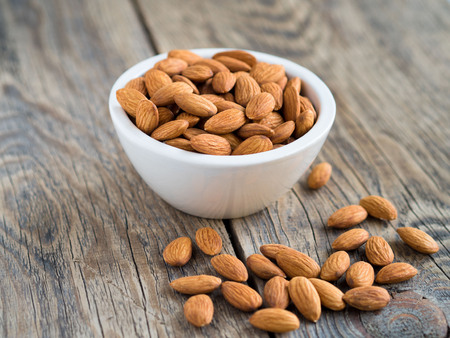 white bowl with a handful of nuts of almonds on a wooden background tableの写真素材