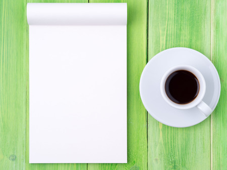 Notepad open with white blank page for writing idea or to-do list, a Cup of coffee  on bright green wood tableの写真素材