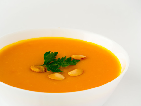 white bowl of pumpkin soup, garnished with parsley and sunflower seeds on a white backgroundの写真素材