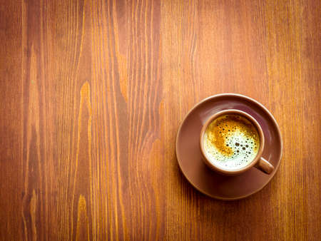 Brown cup of frothy coffee on wooden background. Top view with vignetteの写真素材