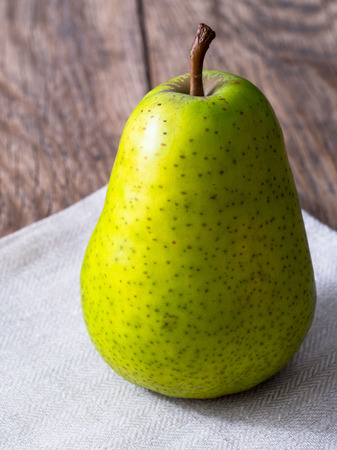 large green pear, one stands on a linen cloth, on a wooden table. Image of a fruit with a shadow.の写真素材