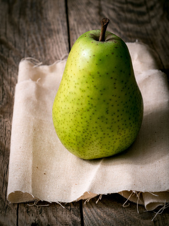 large green pear, one stands on a linen cloth, on a wooden table. An image of a fruit with a shadow in dark tones.の写真素材
