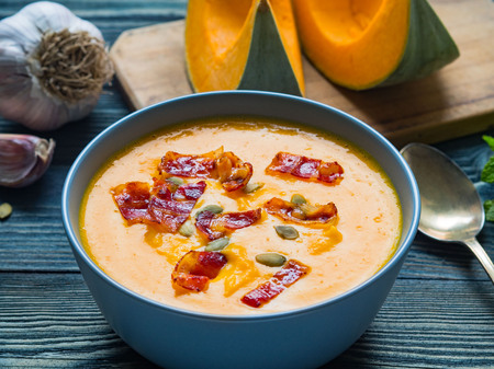 Creamy soup of pumpkin with bacon and seeds on dark blue wooden background, garlic, slices of pumpkin. Side view, close-up, selective focus.の写真素材
