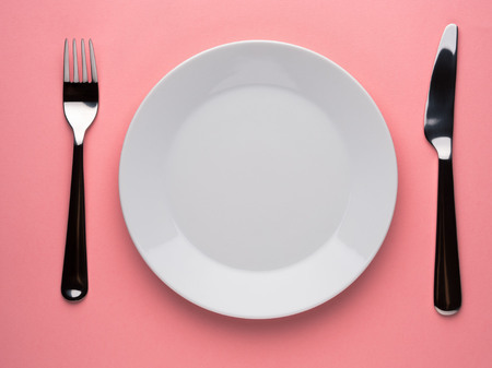 Blank flat plate, knife, fork on a color pink table, top view.の写真素材