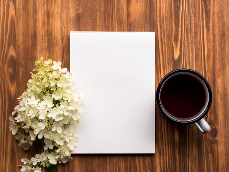 tea Cup, open Notepad with a clean white page and white flower of hydrangea on wooden table, top viewの写真素材