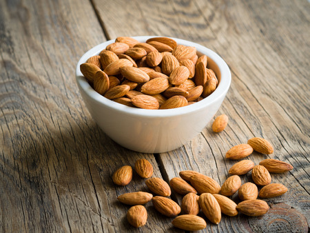 white bowl with a handful of nuts of almonds on a wooden background table. Image with shadow.の写真素材
