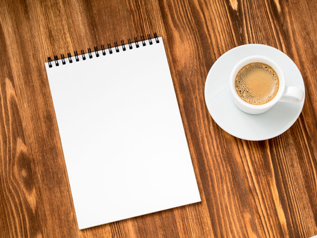 coffee in white cup and open notepad with a clean white page on brown wooden table, top view, diagonalの写真素材