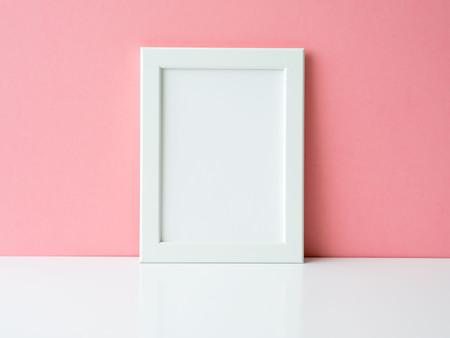 Blank white frame on a white table against the pink wall with copy space