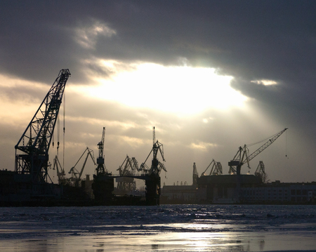 Industrial construction cranes and building silhouettes with sunset on winter  riverの写真素材