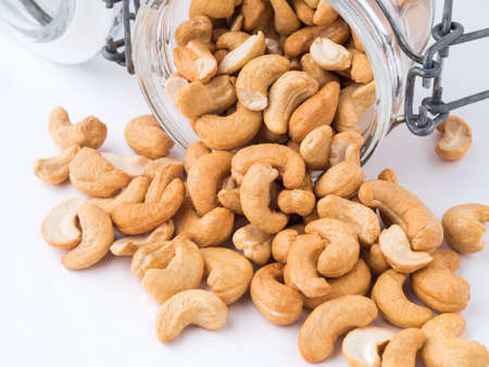 Glass bottle with cashew nuts on white background. A glass bowl with a scattering of nuts, side view,の写真素材
