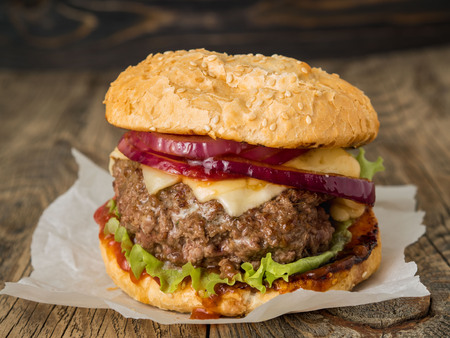 Big delicious homemade burger with beef cutlet, cheese, onion, tomato and lettuce on toasted rolls. American fast food, unhealthy eating.  Side view, selective focusの写真素材