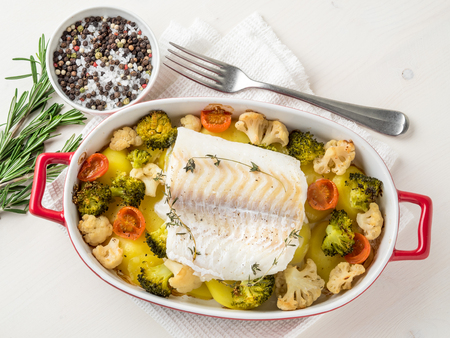 Fish cod baked in the oven with vegetables - healthy diet healthy food. Light white wooden ...
