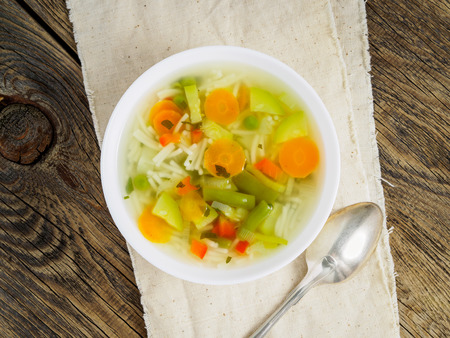 Bright spring vegetable dietary vegetarian soup, linen napkin, top view, wooden background.の写真素材