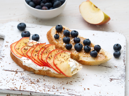 Healthy breakfast with sweet sandwiches - ricotta, blueberries, apple slices, peanut butter on white rustic wood table, side viewの写真素材