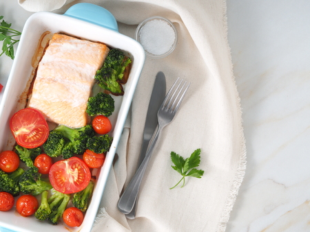 Fish salmon baked in oven with vegetables - broccoli, tomatoes. Healthy diet food, white marble backdrop, top view, close-upの写真素材