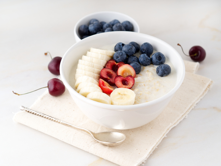 Large bowl of tasty and healthy oatmeal with a fruits and berry for Breakfast, morning meal. Side view, white marble tableの写真素材