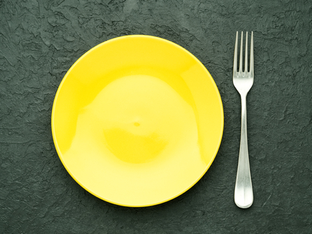 Blank flat yellow plate, fork on dark gray stone concrete table, top view. Mock up, copy spaceの写真素材