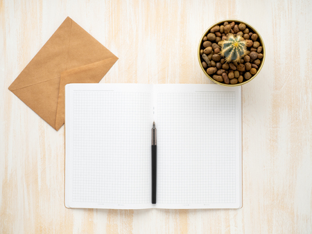 white open notepad, kraft envelope and cactus in pot lying on a beige wooden desk, flat lay, copyspaceの写真素材