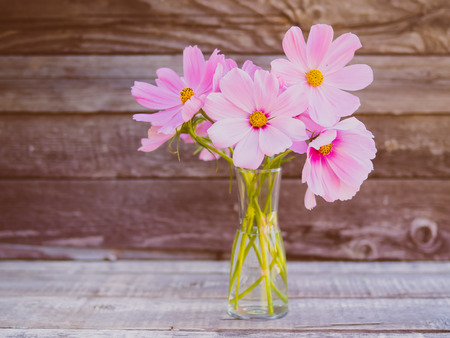 glass vase with a bouquet of pink delicate fragile flowers on wooden background of rough boards, copy space for text.の写真素材