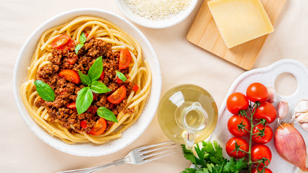 pasta bolognese with tomato sauce, ground minced beef, basil leaves on white table, linen napkin, top view,  long banner formatの写真素材