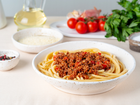 pasta bolognese with tomato sauce, ground minced beef, basil leaves on white table, linen napkin, side viewの写真素材