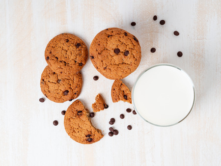 Oatmeal cookies with chocolate drops and milk in glass, healthy snack. Light background, white wooden table, top view.の写真素材
