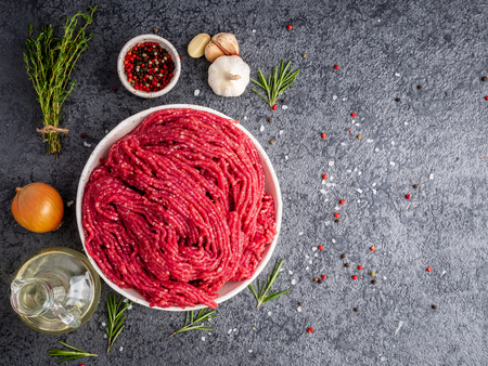Mince beef, ground meat with ingredients for cooking on dark gray background with copy space, top...