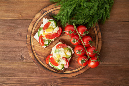 Smorrebrod - traditional Danish sandwiches. Black rye bread with boiled egg, cream cheese, cucumber, tomatoes on dark brown wooden background, top viewの写真素材