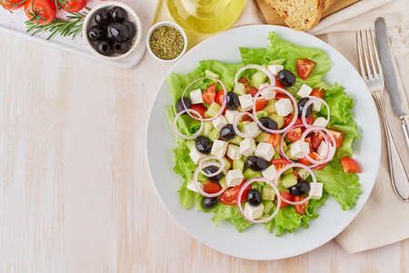 Greek salad on white plate on old rustic white wooden table, fresh salad with tomatoes, cucumbers, feta, onion. Top view, copy spaceの写真素材