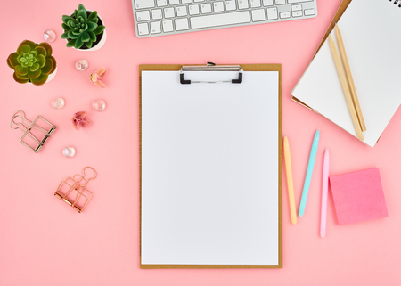 Blank notepad page for text on pink office desktop. Top view of modern bright table with notebook, keyboard. Mock up, copy spaceの写真素材