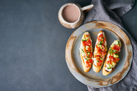 Three crostini, traditional Italian sandwich with tomatoes and cucumbers. Breakfast on plate, Cup of cocoa, copy space, top viewの写真素材